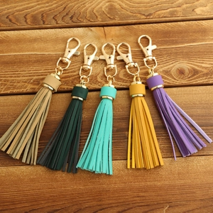 Five suede leather tassels in beige, green and purple with gold lobster clasps on wood