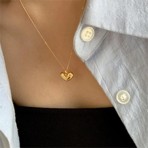 Close-up of a glossy gold heart pendant necklace on a minimalist blue shirt outfit