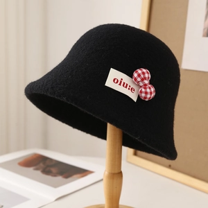 Close-up of black lamb wool bucket hat with a red gingham bow and brand woven label