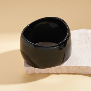 Macro shot of minimalist wide black resin bangle on stone, showcasing glossy finish