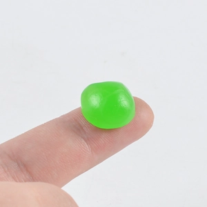 Close-up of a miniature green translucent PVC apple charm held on a fingertip