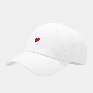 Classic white cotton baseball cap with small red heart embroidery from a side angle view