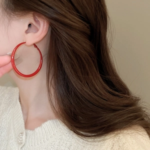 Macro detail of a large red hoop earring with glossy finish worn by a model