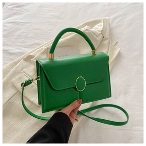 Détail du sac bandoulière en cuir PU vert avec boucle dorée sur literie blanche