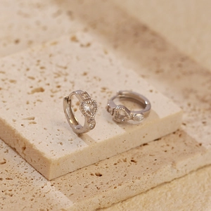 Macro shot of silver S925 heart zircon hoop earrings on textured stone base