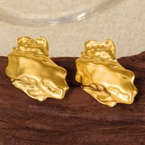 Macro shot of 18K gold earrings with irregular lava texture on dark wood base