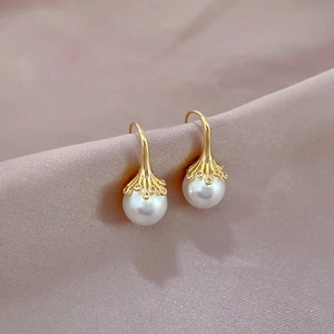 Macro shot of white pearl earrings with golden textured caps on soft satin fabric