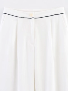 Close-up of white trousers featuring a beige button and black trim detail at the waist