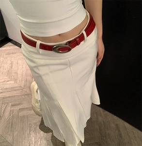 Détail d'une ceinture en cuir rouge croco avec boucle argentée sur une jupe blanche