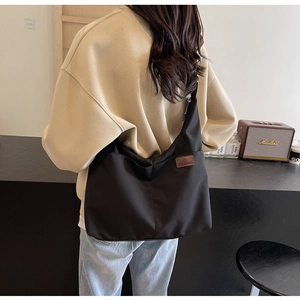 Back view of a model wearing a large black canvas tote bag in a cozy cafe setting