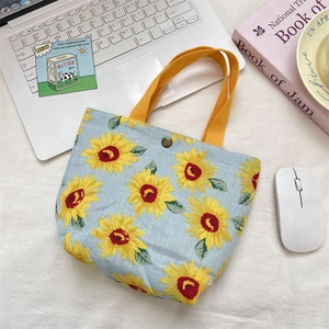 Detail of light blue floral canvas handbag with yellow handles and bronze metal snap button