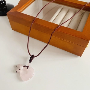 Close-up of pink heart crystal pendant on brown braided rope over wooden box