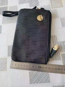 Macro view of a black embossed clutch bag with gold zipper and metal ring detail