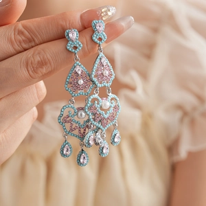 Détail de boucles d'oreilles à pompon argenté avec cœur, goutte et strass multicolores