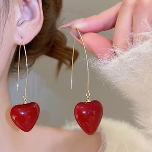 Close-up of elegant gold earrings with glossy red heart pendants worn by a model