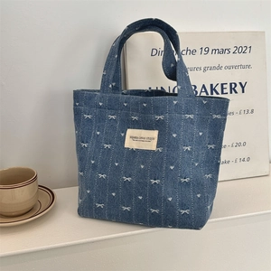 Détail du sac cabas en denim bleu avec motif de nœuds blancs et étiquette en toile