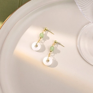 Detail of beaded earrings with green bead and white circular drop on a gold chain