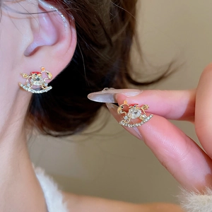 Macro shot of gold rocking horse earrings with crystals and red accents on ear
