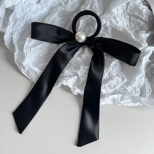 Elegant black satin bow hair tie with a central pearl ornament on white paper