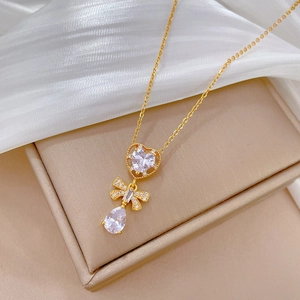 Elegant gold titanium necklace with heart, bow, and teardrop crystals on jewelry box