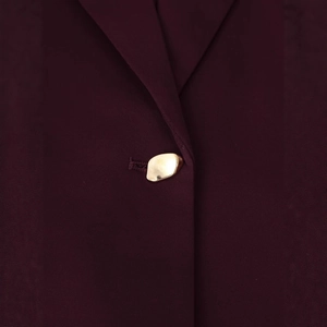 Détail d'un blazer bordeaux avec un bouton doré en métal irrégulier et poli