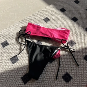 Detailed flat lay of pink bandeau bikini top and black side-tie bottoms on textured rug