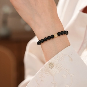 Close-up of obsidian bead bracelet with translucent yellow gem on wrist with white embroidery