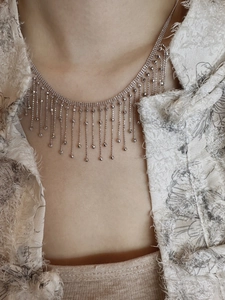 Close-up of a silver tassel necklace featuring delicate beaded chains on a tweed jacket