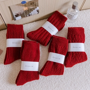 Five pairs of thick red knitted wool socks with textured diamond patterns on white faux fur