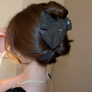 Close-up of a large black fabric bow hair claw with gold rhinestones on model's hair