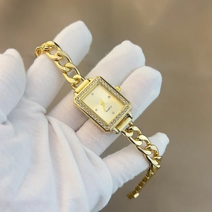 Macro shot of rectangular gold women's watch with rhinestone bezel and chain bracelet