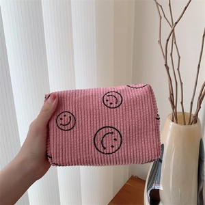 Detail view of a pink corduroy makeup bag featuring three hand-drawn smiley faces