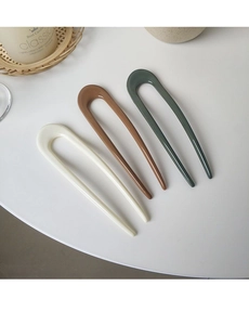 Close-up of three colorful U-shaped hair pins on marble surface for stylish bun hairstyles