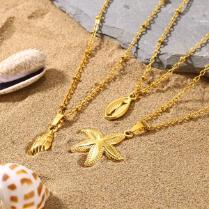 Golden seashell, starfish, and conch shell pendant ball chain necklaces on beach sand