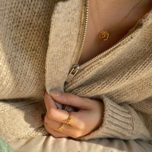 Elegant gold knot ring and triple ring pendant necklace on model with beige sweater