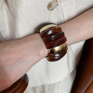 Close-up of a wide amber acrylic resin cuff bracelet with polished gold metal links