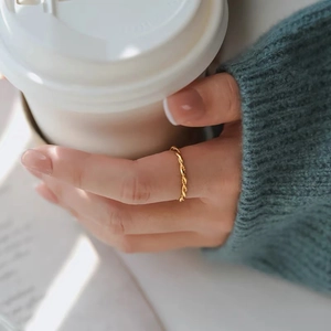 Detail of a thin gold twisted rope ring worn by a model against a cozy sweater background