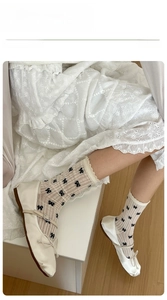Detail view of ballet-style beige mid-calf socks with black bows and lace trim edges