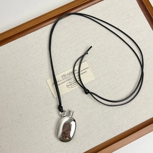 Detailed view of oval polished metal pebble pendant with black cord on a wooden tray