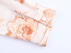 Dettaglio macro del polsino ricamato beige con motivi floreali e un bottone bianco