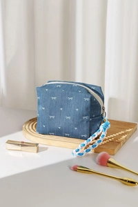 Detail of denim makeup bag with white bows and colorful woven strap on white background