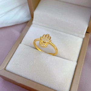 Golden Hamsa hand ring with white zircons on a beige velvet jewelry box surface