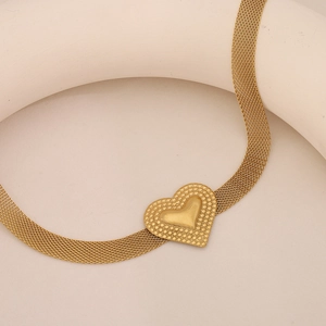 Detail shot of golden mesh chain necklace with textured heart pendant on beige background