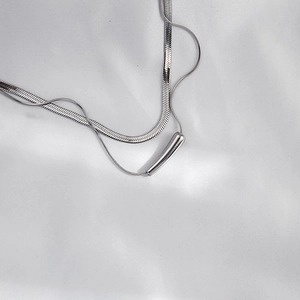Double-layer silver snake chain necklace with cylindrical pendant on white silk fabric