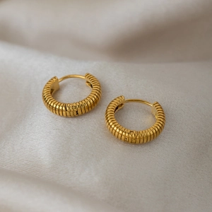 Close-up of golden stainless steel hoop earrings with textured horizontal stripes on fabric