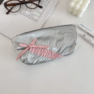 Modern silver crinkled pencil case with pink bow detail shown in a cozy desktop scene