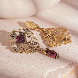 Macro detail of vintage gold floral earrings with purple heart resin and drop crystal
