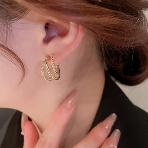 Elegant multi-layer C-shape gold earrings with sparkling diamonds on a female model