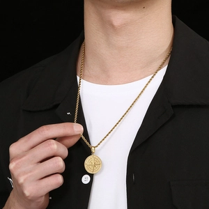 Gros plan d'un pendentif boussole doré avec chaîne torsadée porté par un homme