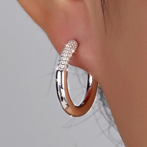 Detailed view of silver hoop earrings with white zircon stones worn on the ear